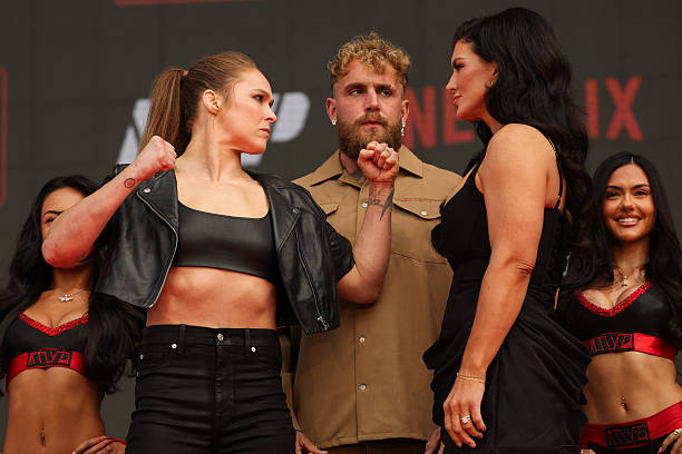 Ronda Rousey (L) and Gina Carano (R) face off in front of Jake Paul (C)